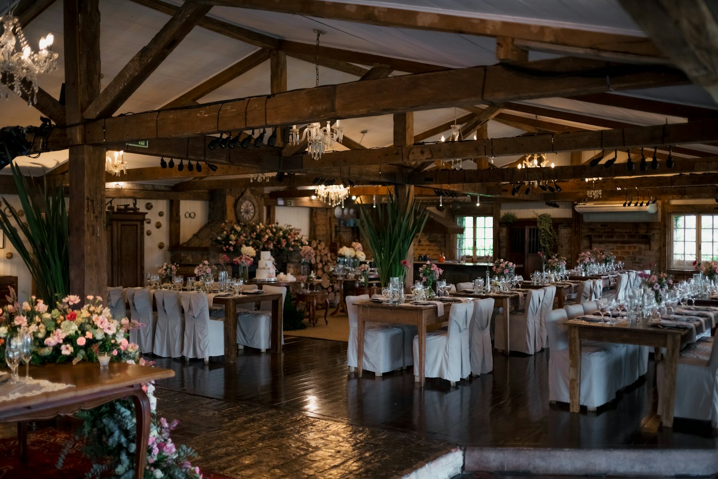 Veranstaltungsraum mit Holztischen, Blumengestecken und Kronleuchtern.