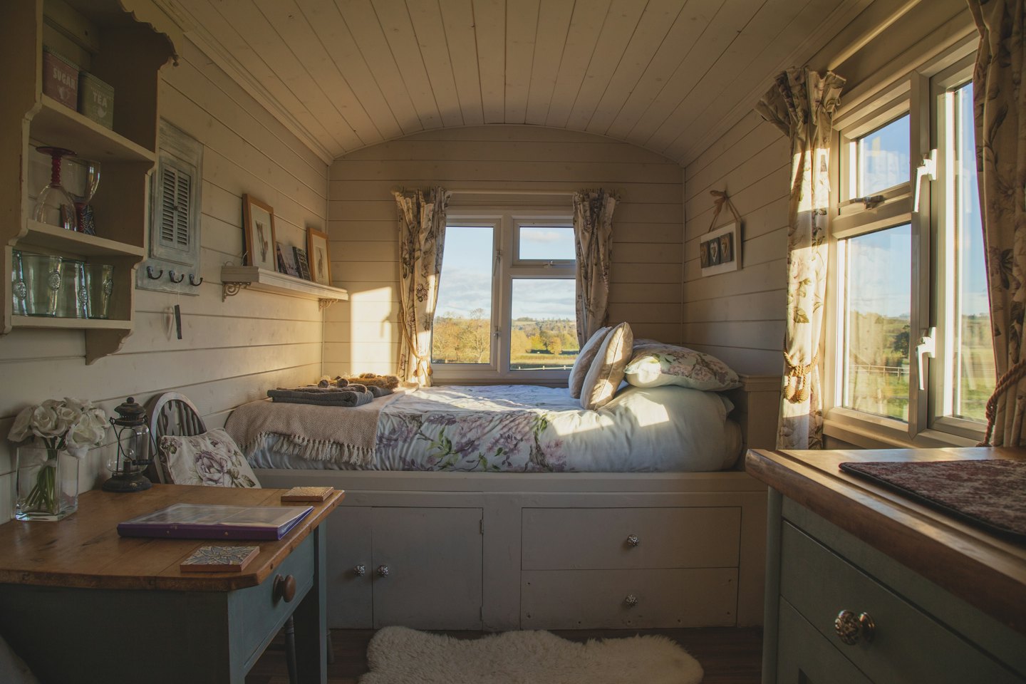 Gemütlicher Wohnraum in einer Hütte mit Bett, Schreibtisch und Sonnenschein.