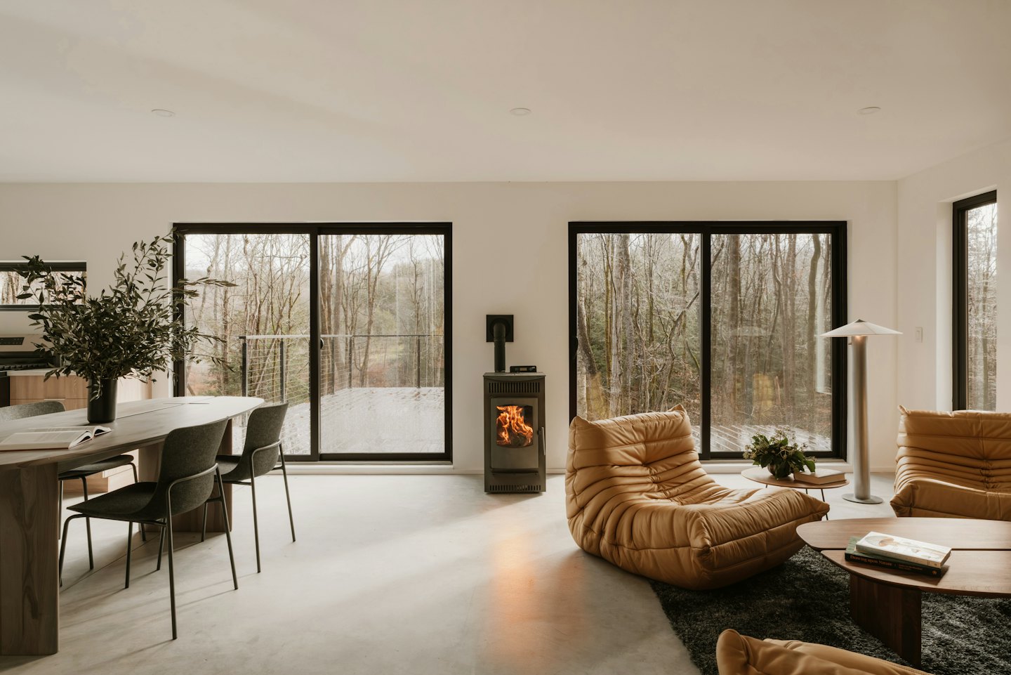 Modernes Wohnzimmer mit großen Fenstern und Blick auf einen verschneiten Wald.
