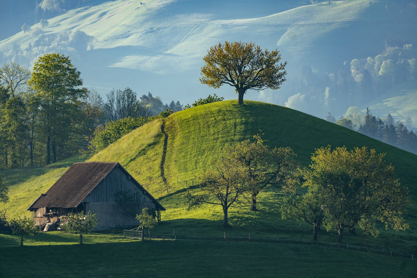 Eine rustikale Holzhütte liegt unter sanften grünen Hügeln.