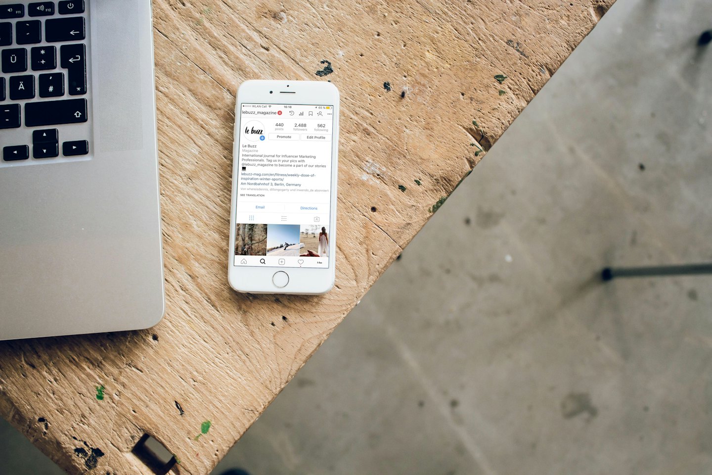 Smartphone mit geöffnetem Instagram auf einem Holztisch neben einem Laptop.